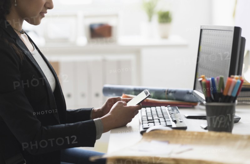 Mixed race businesswoman using cell phone at desk