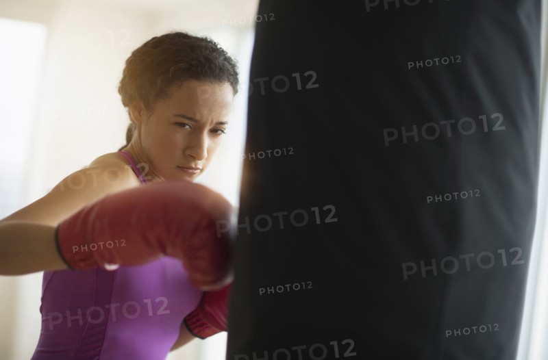Mixed race woman hitting punching bag in gym