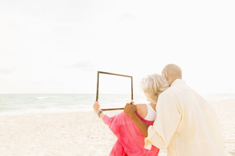 Older couple holding empty picture frame on beach