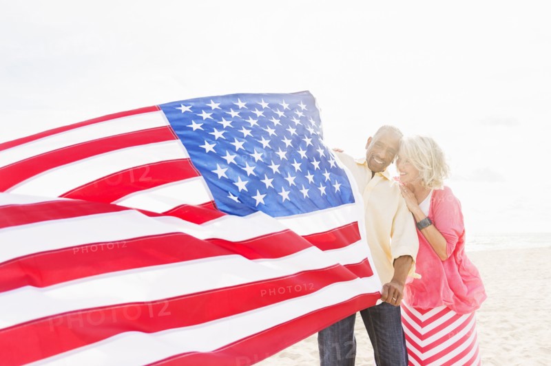 Older couple holding American flag on beach