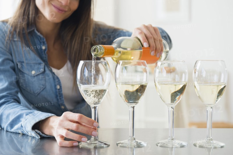 Caucasian woman pouring glasses of white wine