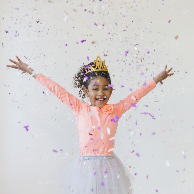 Mixed race girl wearing tiara throwing confetti