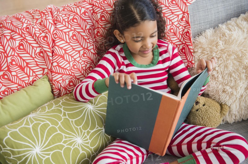 Mixed race girl reading book on sofa