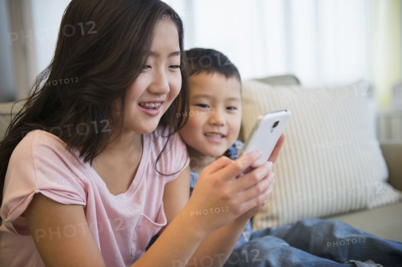 Asian brother and sister using cell phone on sofa