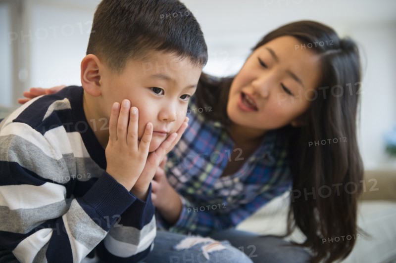 Asian sister comforting sad brother on sofa