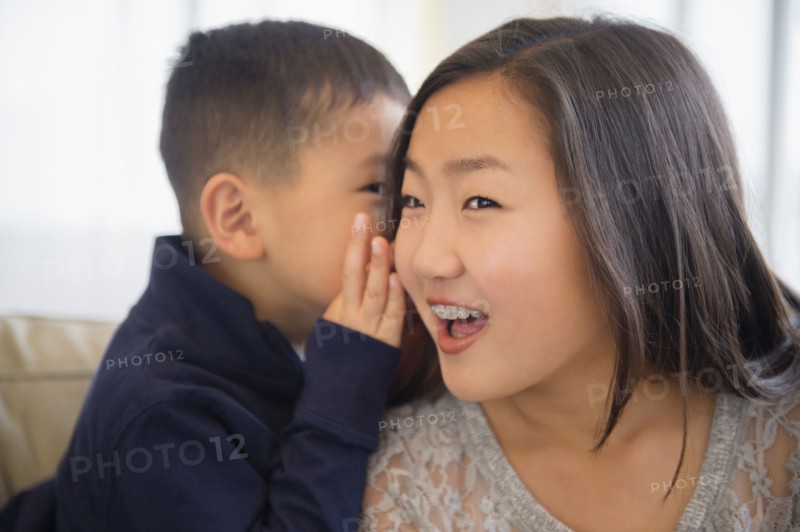 Asian boy whispering in ear of sister