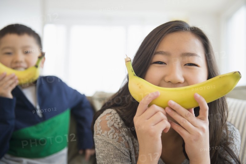 Asian children holding bananas in front of faces for smiles