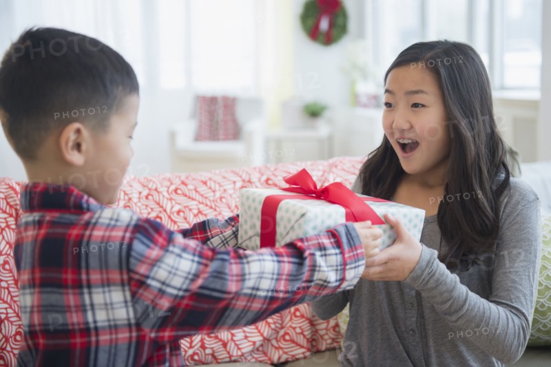 Asian brother giving sister Christmas gift in living room