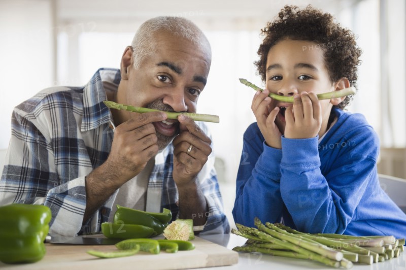 Mixed race grandfather and grandson making mustaches with asparagus
