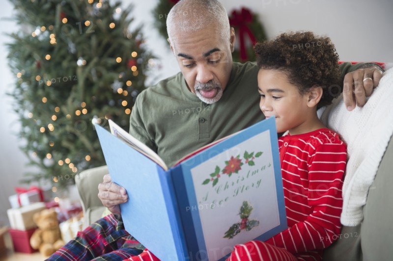 Mixed race grandfather reading to grandson at Christmas