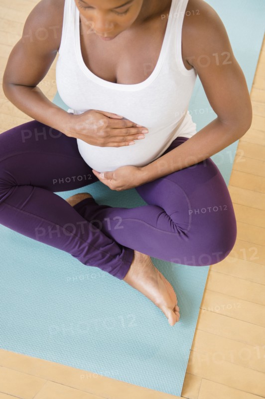 Black pregnant woman sitting on exercise mat holding stomach