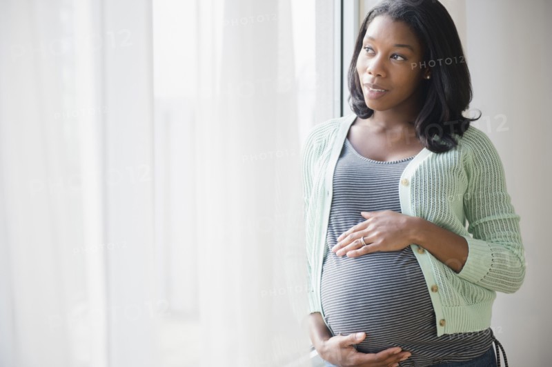 Black pregnant woman holding her stomach at window