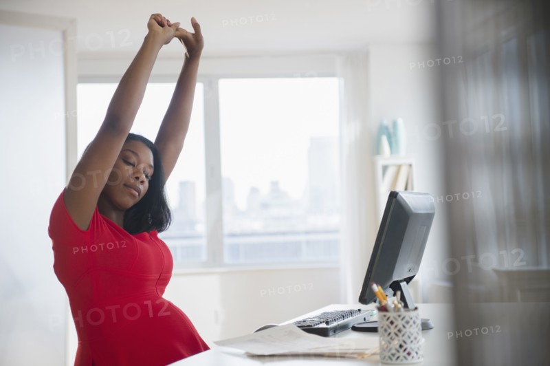 Black pregnant businesswoman stretching arms at desk in office