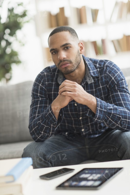 Hispanic man with cell phone and digital tablet in living room