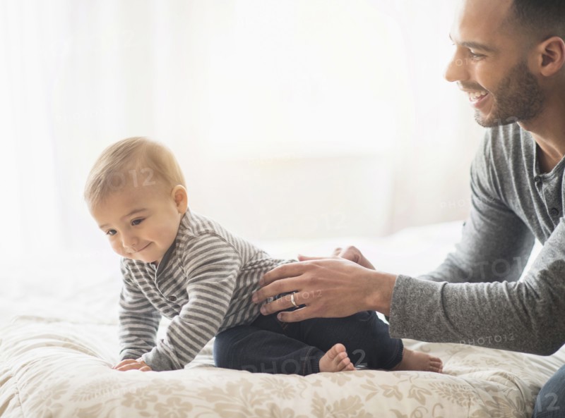 Father playing with baby son on bed