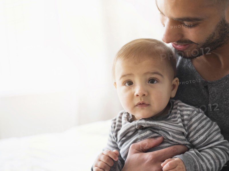Smiling father holding baby son on bed