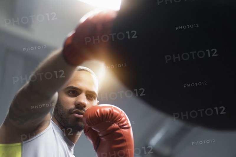 Close up of Hispanic man punching bag in gym
