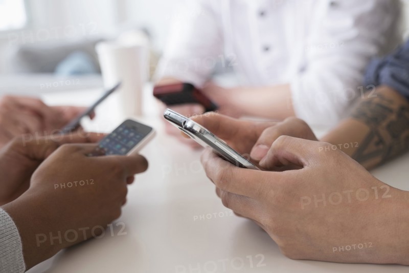 Close up of friends texting with cell phones at table