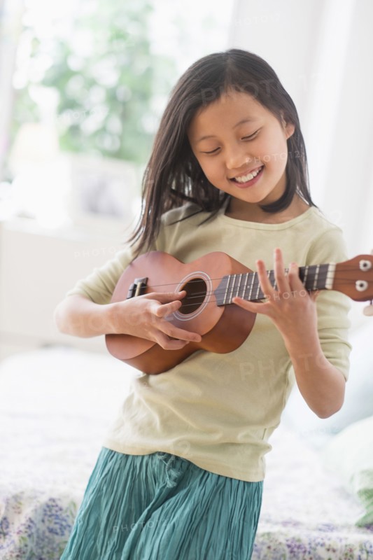 Chinese girl practicing ukulele in bedroom