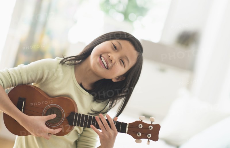 Chinese girl practicing ukulele in bedroom