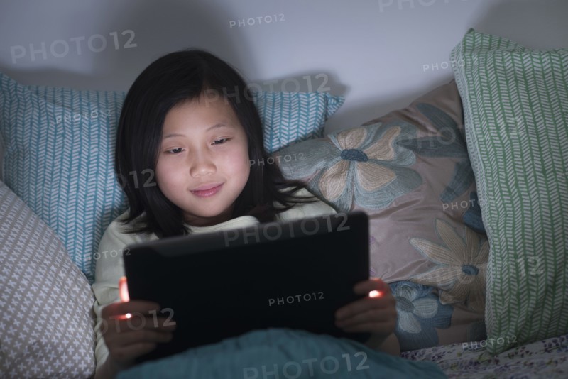 Smiling Chinese girl watching digital tablet in bed