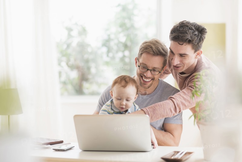 Caucasian gay fathers and baby using laptop