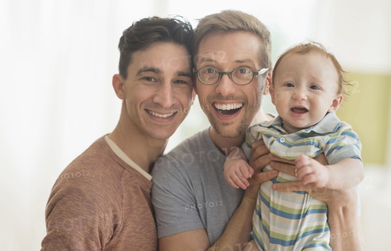 Smiling Caucasian gay fathers holding baby