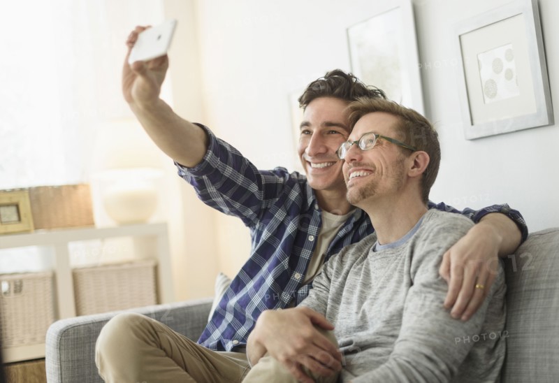 Caucasian gay couple taking selfie on sofa