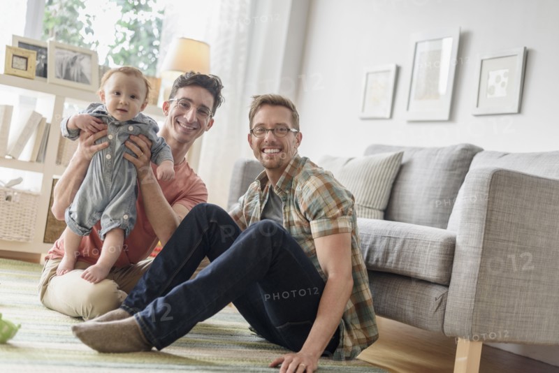 Caucasian gay fathers and baby playing in living room