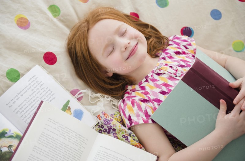 Caucasian girl reading books on bed