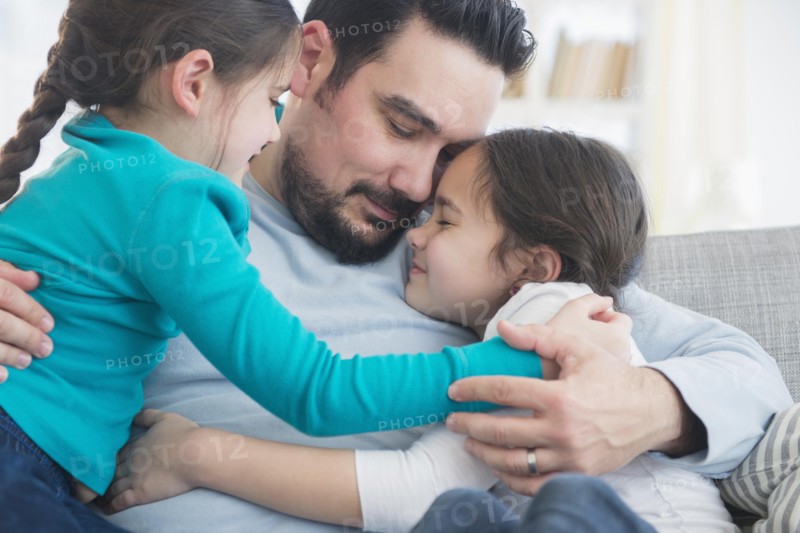 Caucasian father and daughters hugging on sofa