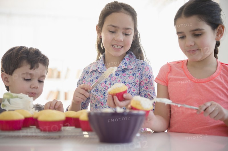 Caucasian siblings spreading frosting on cupcakes