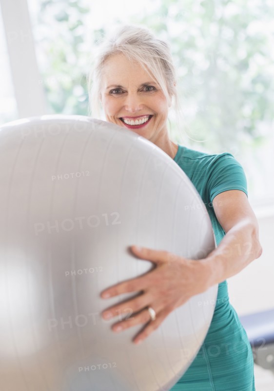 Older Caucasian woman holding exercise ball in gym