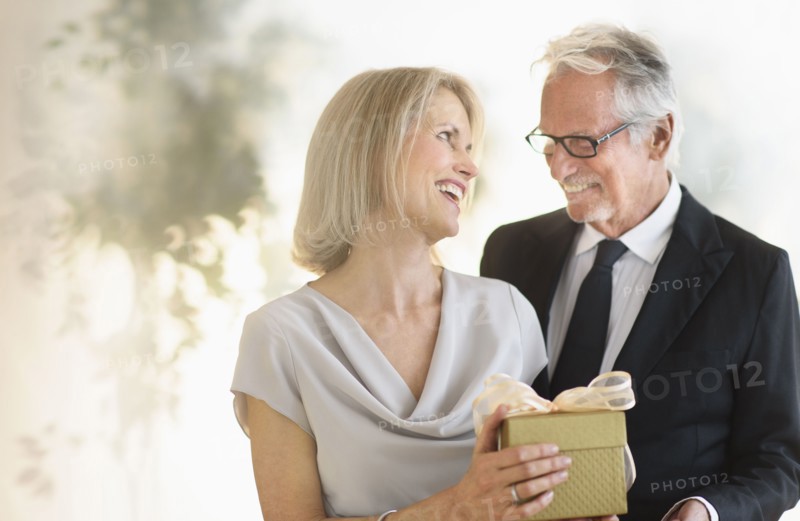 Smiling older Caucasian man giving wife a gift