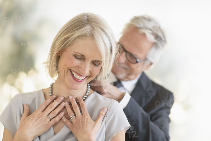 Smiling older Caucasian man giving wife a necklace