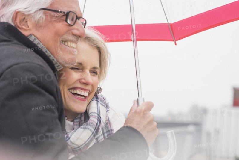 Older Caucasian couple standing under umbrella