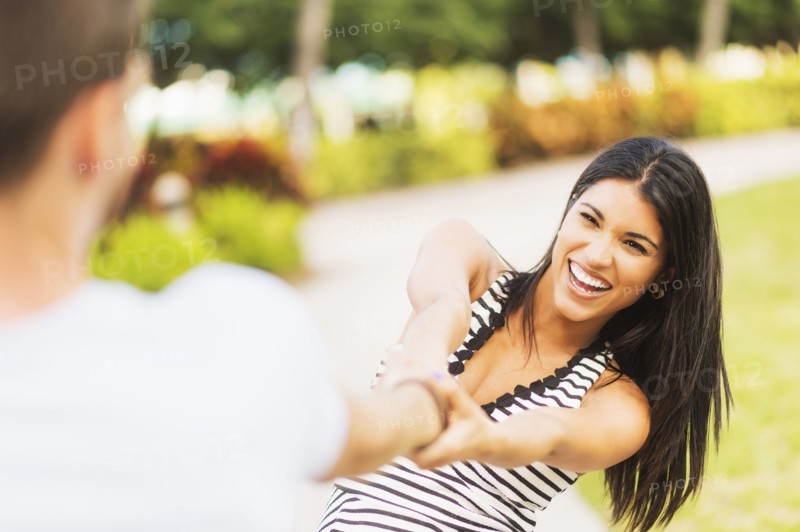 Smiling Hispanic woman pulling boyfriend in park
