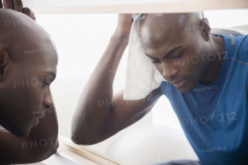 Black man resting near mirror after workout
