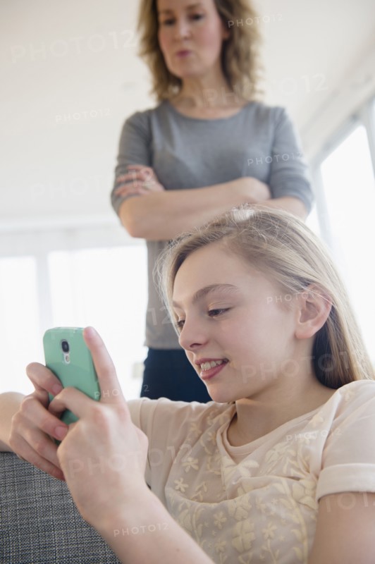 Caucasian mother watching daughter use cell phone