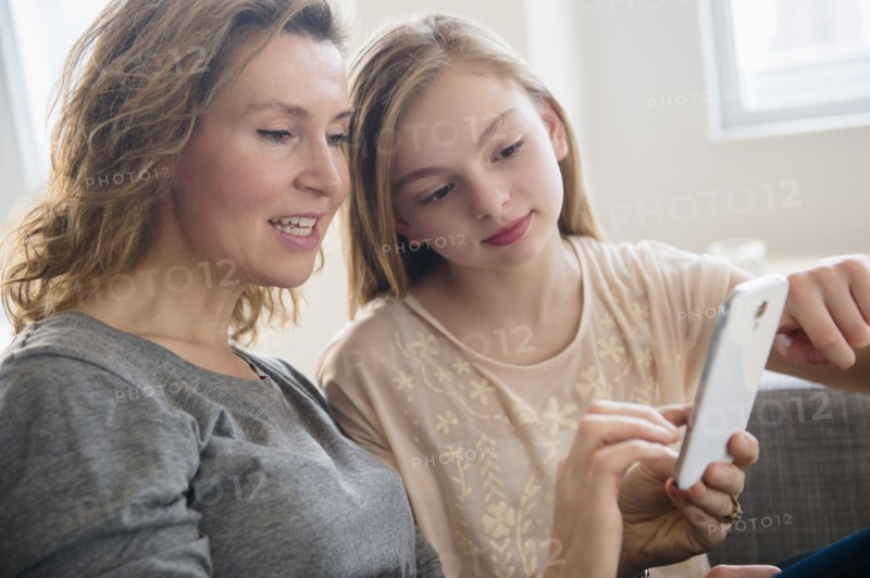 Caucasian mother and daughter using cell phone in living room