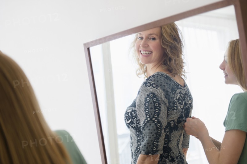Caucasian daughter zipping dress for mother