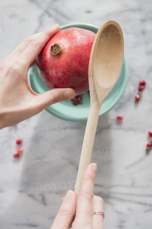 Close up of hands cracking pomegranate with spoon