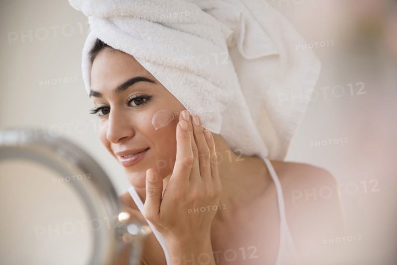 Woman with hair in towel rubbing lotion on face