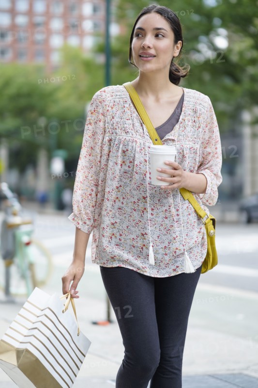 Hispanic woman carrying shopping bag on city sidewalk