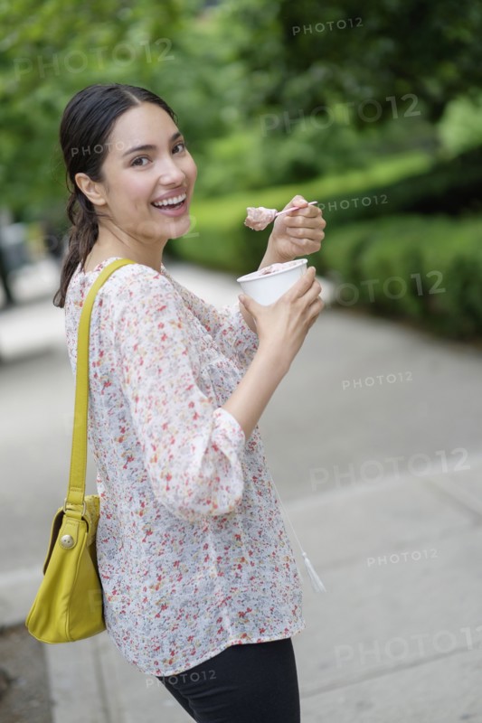 Hispanic woman eating frozen yogurt on city sidewalk