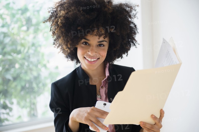 Mixed race businesswoman using cell phone near window