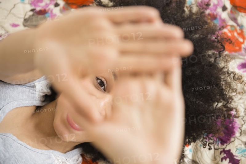 Mixed race woman peering through fingers on bed