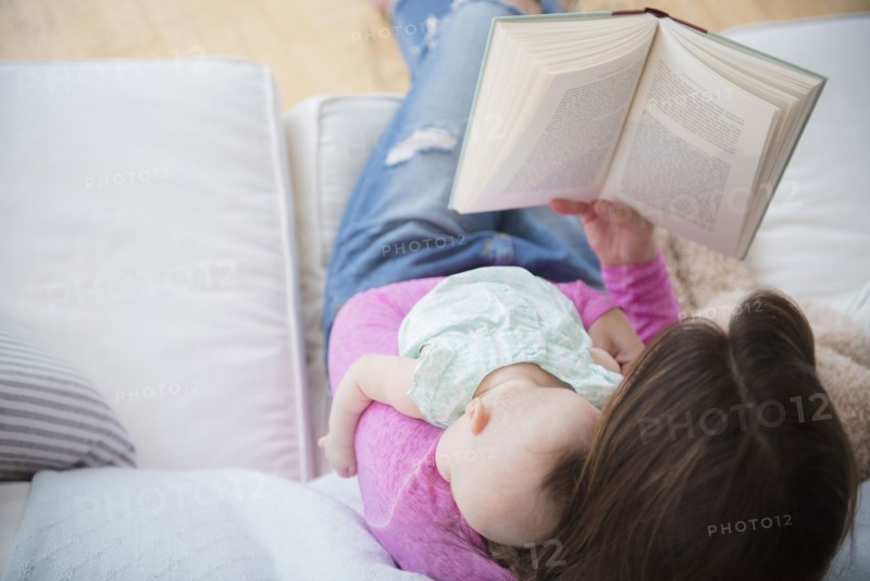 Mother reading book and holding baby daughter