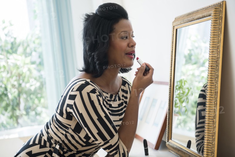 Black woman applying lipstick in mirror