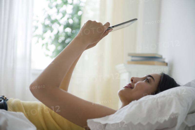 Hispanic woman using digital tablet in bed
